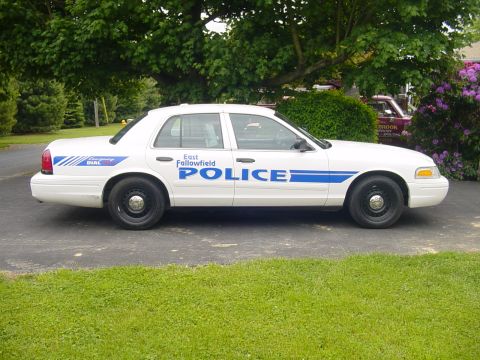 2002 Ford Crown Victoria - Side view of a white 2002 Ford Crown Victoria police car with 'East Fallowfield POLICE' text and blue stripes.