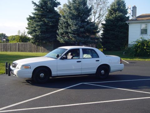 2002 Ford Crown Victoria - This white sedan is parked in a lot with trees and a house in the background.