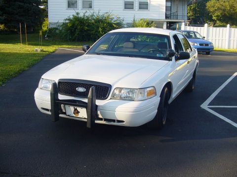 2002 Ford Crown Victoria - A white 2002 Ford Crown Victoria is parked in a driveway, with a blue car visible in the background.