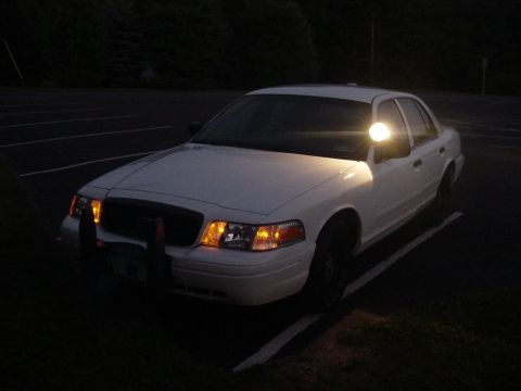 2002 Ford Crown Victoria - A white 2002 Ford Crown Victoria is parked in a lot at night, with its spotlight illuminated.
