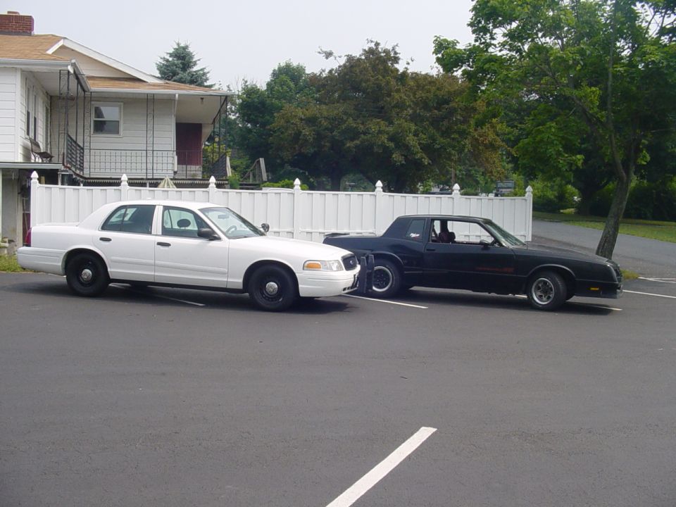 White Ford Crown Victoria sedan parked beside black Chevrolet Monte Carlo coupe in lot