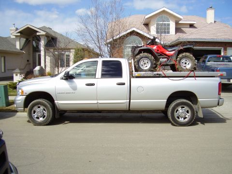 2005 Dodge 3500 - A silver 2005 Dodge 3500 pickup truck is parked on a residential street, carrying a red ATV on its flatbed.