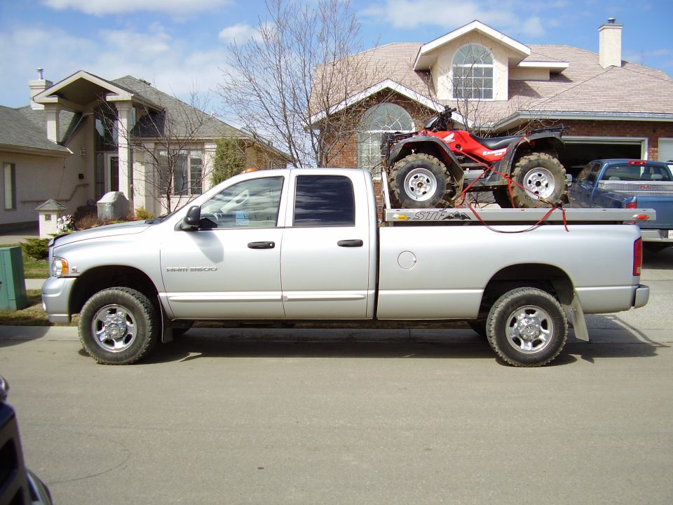 Silver 2005 Dodge 3500 pickup truck, side view, carrying a red ATV on a flatbed