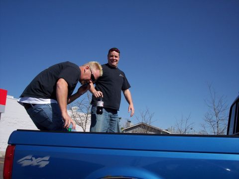 1972 Ford Ranchero - Two men are in the bed of a blue pickup truck on a sunny day.