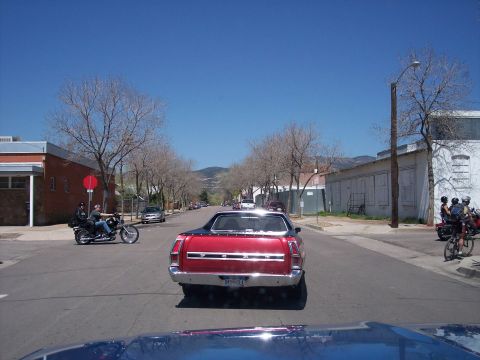 1972 Ford Ranchero - A red pickup truck is seen from behind on a street with other vehicles and pedestrians.