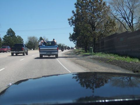 1972 Ford Ranchero - A convoy of motorcycles follows a blue pickup truck carrying passengers on a sunny day.