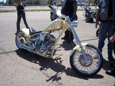 1972 Ford Ranchero - A custom chopper motorcycle with a cream paint job and flame pinstriping is parked on asphalt with other motorcycles and people around.