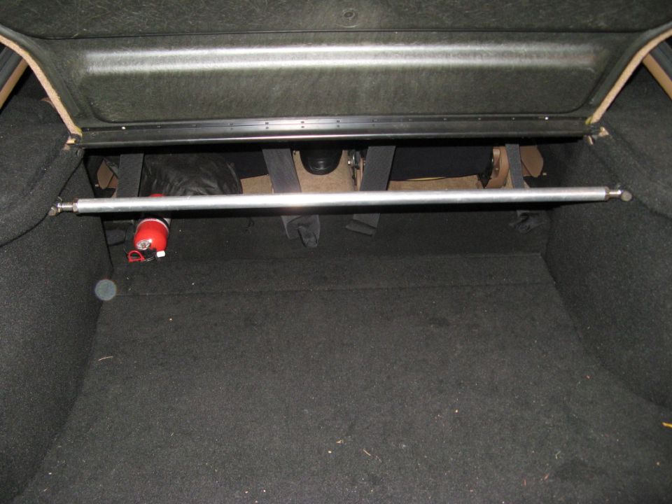 Car trunk interior with a silver strut bar across the top and a red fire extinguisher mounted on the left