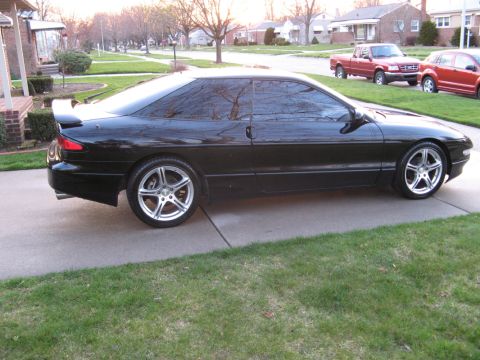 1995 Ford Probe - A black 1995 Ford Probe is parked on a driveway in front of a suburban house.