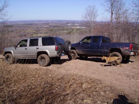 2000 Chevrolet Tahoe - A silver 2000 Chevrolet Tahoe and a blue pickup truck are parked on a dirt trail overlooking a valley, with a dog in the foreground.