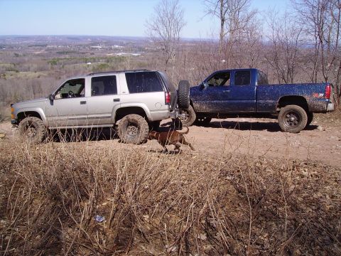 2000 Chevrolet Tahoe - Two trucks parked on a dirt road with a dog running between them, overlooking a valley.