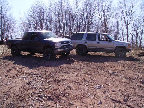2000 Chevrolet Tahoe - Two SUVs are parked on a dirt road with trees in the background.