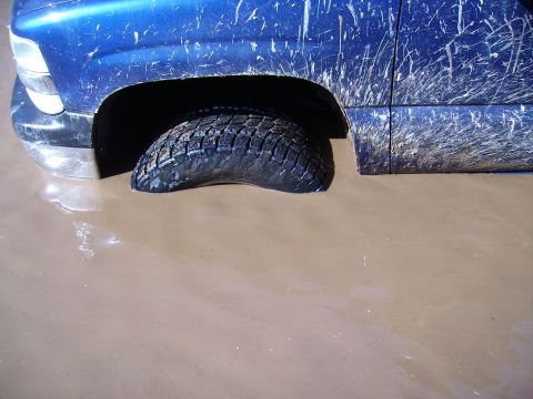 2000 Chevrolet Tahoe - A blue SUV is stuck in mud, with its front tire submerged.