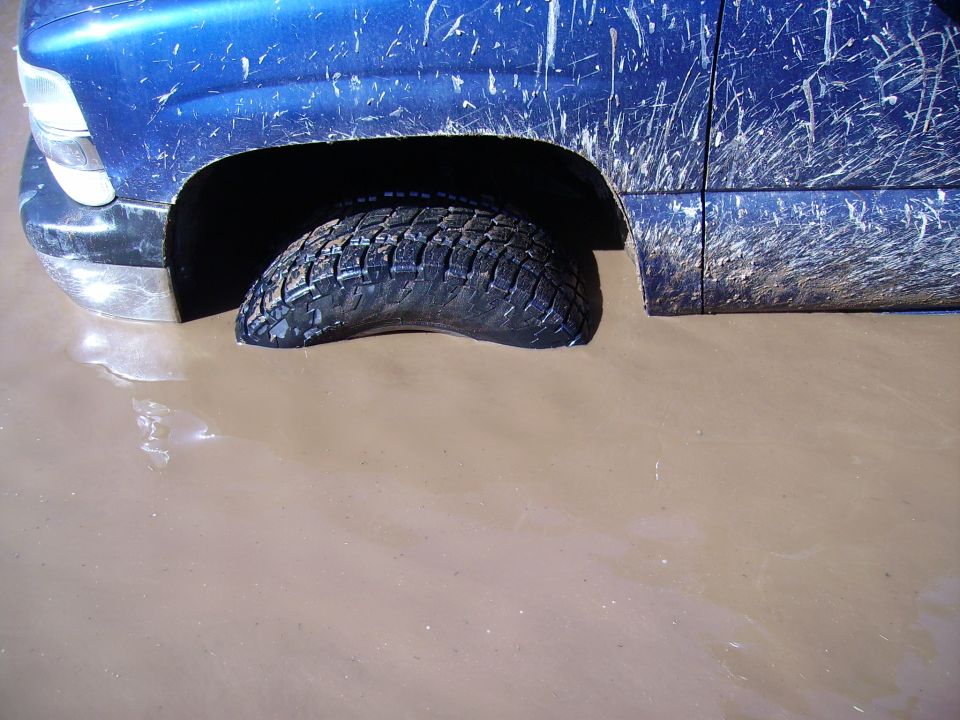 Blue SUV stuck in mud, front fender and tire visible
