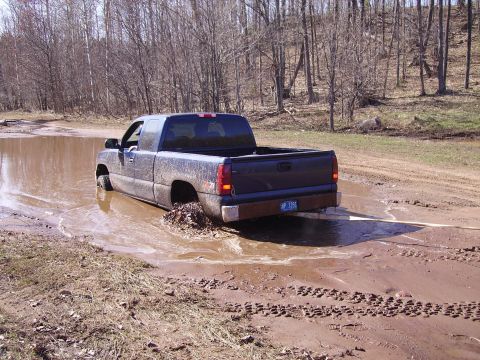 2000 Chevrolet Tahoe - A dark pickup truck is stuck in a muddy area with trees in the background.