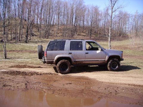2000 Chevrolet Tahoe - SUV navigates a muddy off-road course with trees in the background.