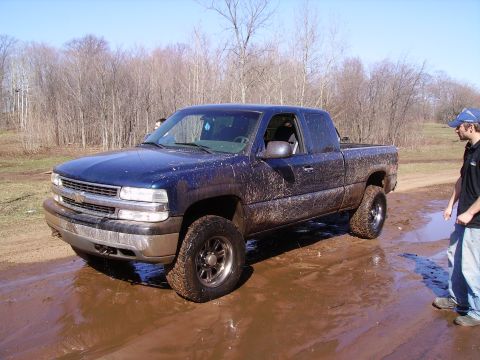 2000 Chevrolet Tahoe - A muddy blue pickup truck sits in a wet, outdoor environment with trees in the background.