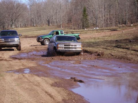 2000 Chevrolet Tahoe - A gray SUV navigates a muddy obstacle course, with two other trucks visible in the background.