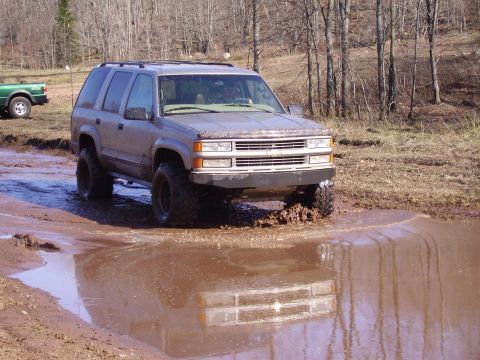 2000 Chevrolet Tahoe - Lifted Chevrolet Tahoe navigating a muddy off-road course with another vehicle nearby.