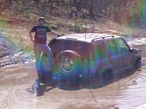 2000 Chevrolet Tahoe - A person stands next to a dark SUV that is stuck in a muddy area.