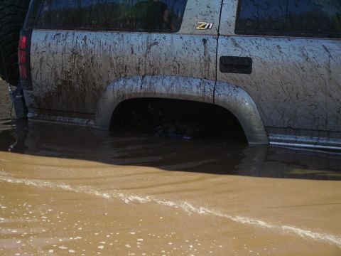2000 Chevrolet Tahoe - A mud-covered SUV, identified as a 2000 Chevrolet Tahoe, is partially submerged in murky water.