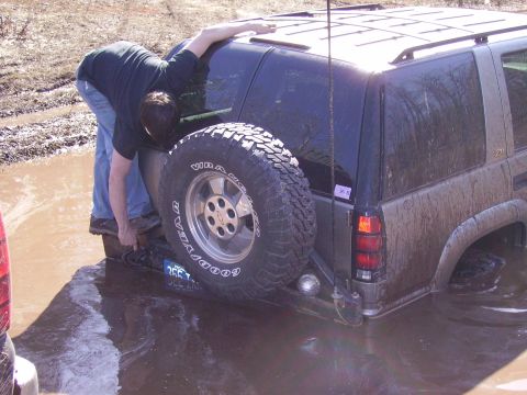 2000 Chevrolet Tahoe - A person attempts to free a mud-covered SUV stuck in a water-filled ditch.