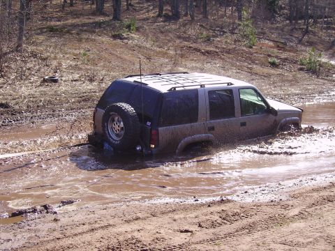 2000 Chevrolet Tahoe - SUV is stuck in a muddy puddle with water splashing around it.