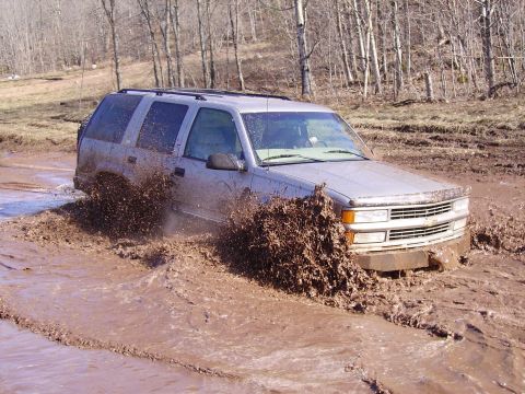 2000 Chevrolet Tahoe - This SUV is navigating a challenging muddy terrain, with significant splashing.