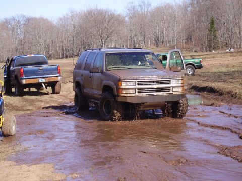 2000 Chevrolet Tahoe - A muddy Chevrolet Tahoe navigates a wet, off-road course with other vehicles present.