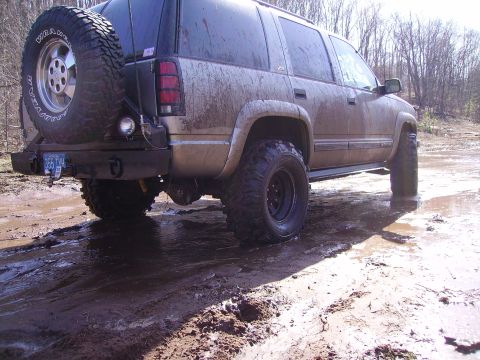 2000 Chevrolet Tahoe - Muddy SUV with spare tire on back, seen off-road.
