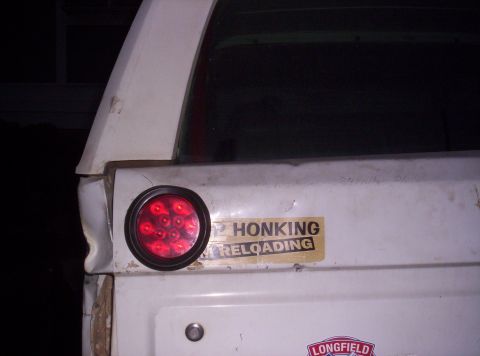 1995 Ford Bronco - The rear of a white SUV shows a damaged tailgate with a sticker and a modern LED taillight.