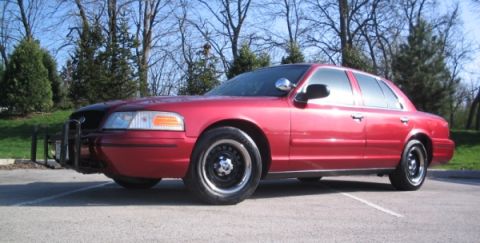 2001 Ford Crown Victoria - A red 2001 Ford Crown Victoria is parked in a lot with trees in the background.