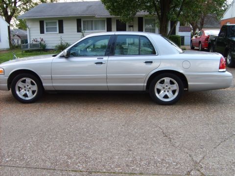 1993 Ford Crown Victoria - Side view of a silver sedan parked on a gravel driveway with a house in the background.