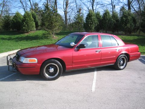 2001 Ford Crown Victoria - A red 2001 Ford Crown Victoria sedan is parked in a lot, a push bumper on the front.