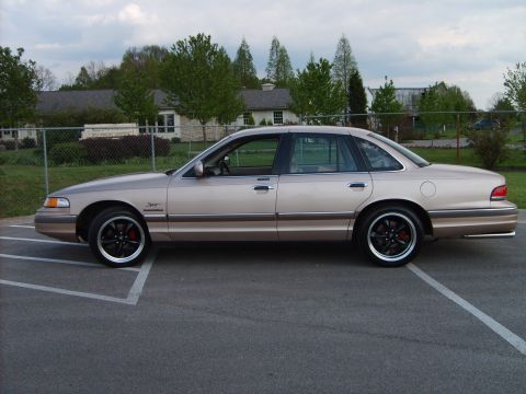 1993 Ford Crown Victoria - This tan Ford Crown Victoria features aftermarket black wheels with red brake calipers, parked outdoors.