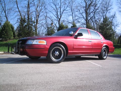2001 Ford Crown Victoria - This red sedan, possibly a 2001 Ford Crown Victoria, is parked in a lot with trees in the background.