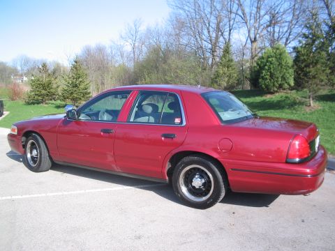 2001 Ford Crown Victoria - Red 2001 Ford Crown Victoria sedan parked on asphalt with trees in the background.