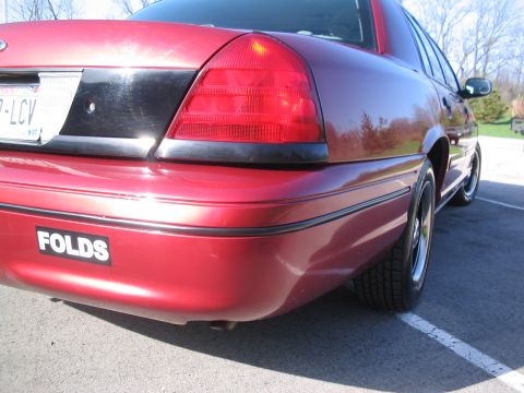 2001 Ford Crown Victoria - Rear view of a red 2001 Ford Crown Victoria sedan, showing the taillight and a bumper sticker.