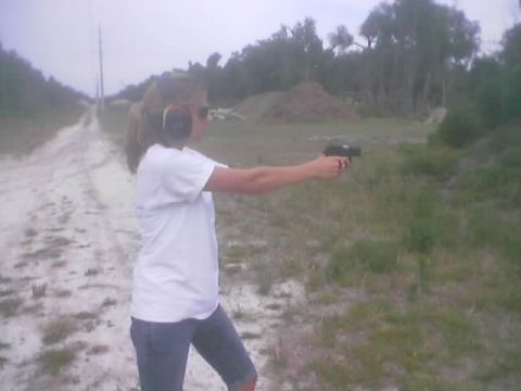1989 Ford Bronco - A woman practices shooting a handgun at an outdoor range with a dirt path and trees in the background.