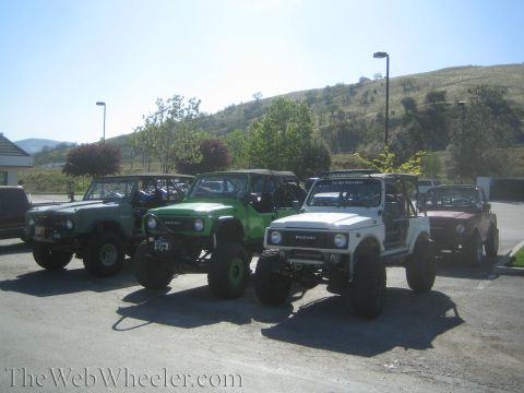 1987 Suzuki Samurai - Several modified off-road vehicles are parked side-by-side in a paved lot under a clear sky.