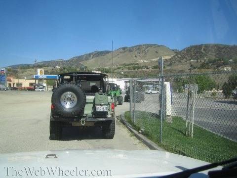 1987 Suzuki Samurai - Several off-road vehicles are lined up at a gas station on a sunny day.