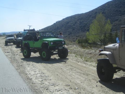 1987 Suzuki Samurai - A line of off-road vehicles, including a green 1987 Suzuki Samurai, are parked on a dusty roadside.