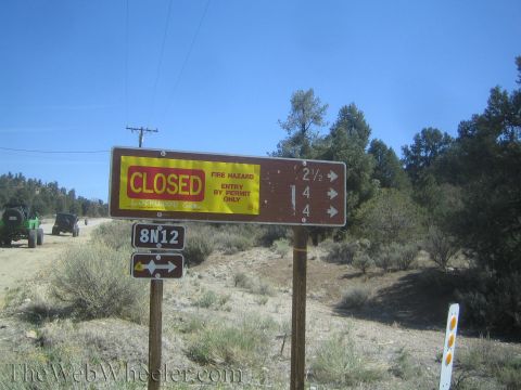 1987 Suzuki Samurai - Two off-road vehicles are seen on a dirt road next to a sign indicating the area is closed due to fire hazard.
