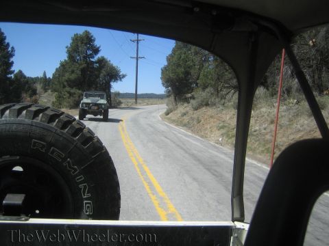 1987 Suzuki Samurai - Driver's POV through a Jeep showing the spare Remington tire and a Jeep ahead on a country road.