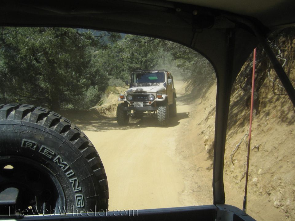 Toyota Land Cruiser FJ40 in front of another off-road vehicle on a dusty dirt road