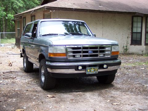 1996 Ford Bronco - This Ford Bronco is parked in front of a weathered house with trees in the background.