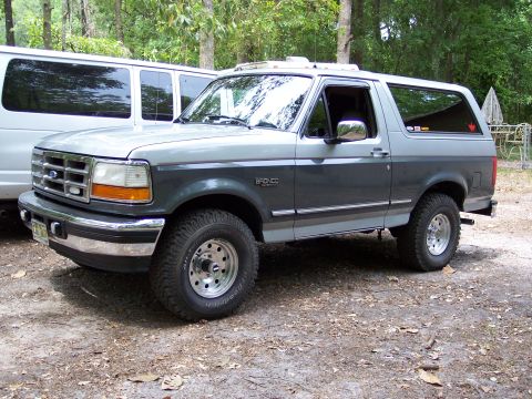 1996 Ford Bronco - A 1996 Ford Bronco is parked outdoors next to a white van, with trees in the background.