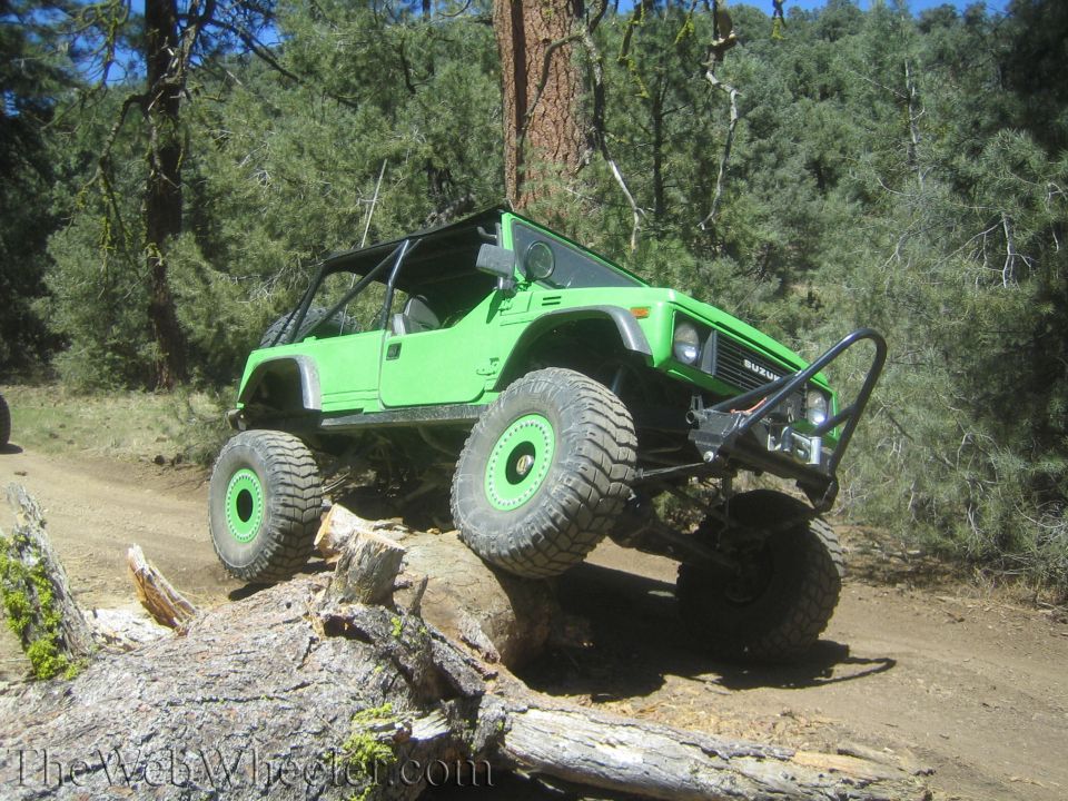 Green 1987 Suzuki Samurai with large off-road tires climbing over a log