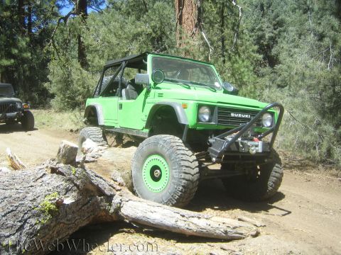 1987 Suzuki Samurai - A modified Suzuki Samurai navigates an obstacle on a wooded trail, with another off-road vehicle in the distance.