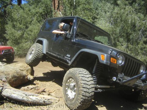 1987 Suzuki Samurai - A black Jeep Wrangler navigates an obstacle on an off-road trail, with a red Suzuki Samurai visible behind it.